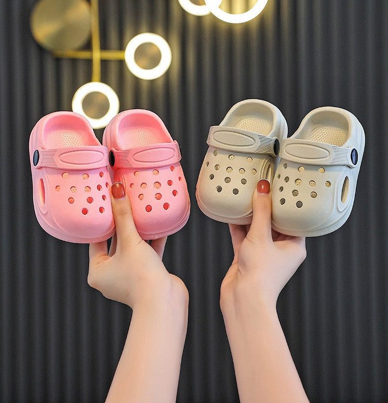 Two pairs of children's shoes held by hands against a dark background with decorative lights.
