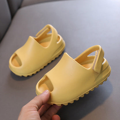 Yellow children's flip-flops on a gray surface with a hand holding one shoe.