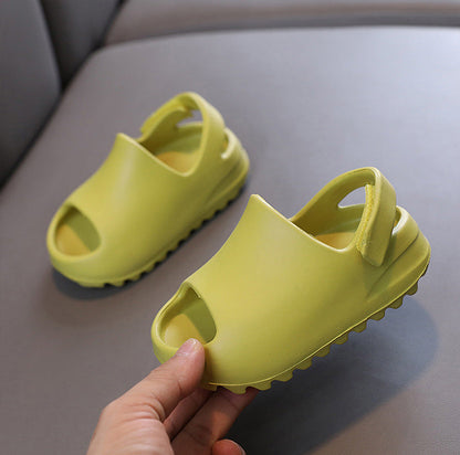 A pair of bright yellow-green children's flip-flop sandals, with one being held by a hand to show the sole and heel detail against a gray background.